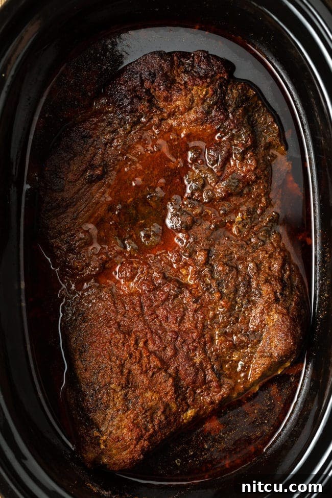 Perfectly cooked and tender brisket resting in the crock pot after hours of slow cooking, ready to be removed.