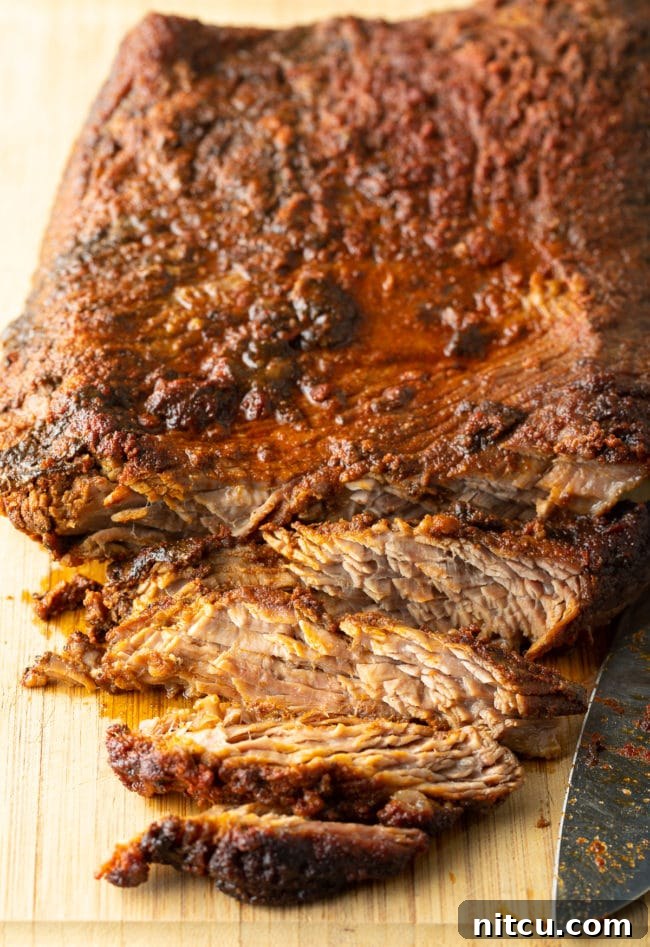 Cooked brisket sliced into thin strips against the grain on a cutting board, before being chopped.