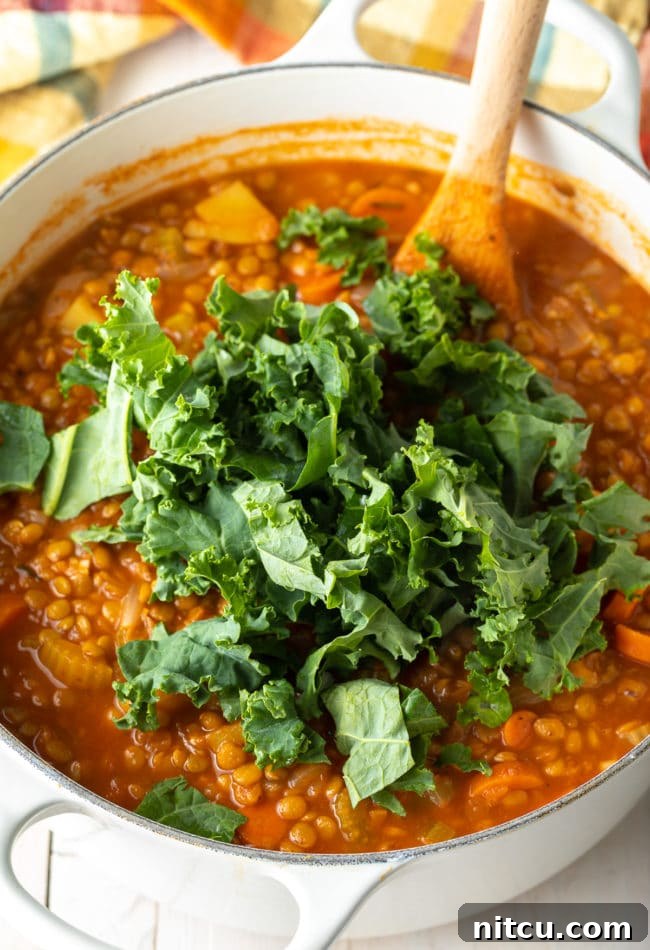 Adding fresh kale to the Tuscan Lentil Soup, a final touch for a healthy and flavorful dish.