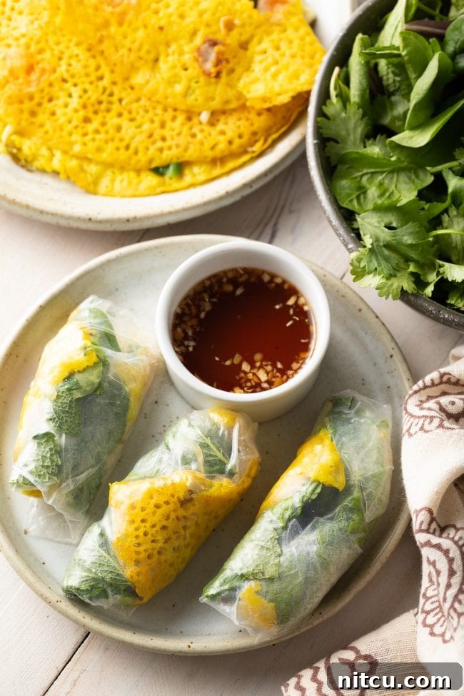 A beautifully composed top-down shot of three Bánh Xèo crepes, each delicately wrapped in transparent rice paper, accompanied by a small ramekin of savory Nuoc Cham dipping sauce.