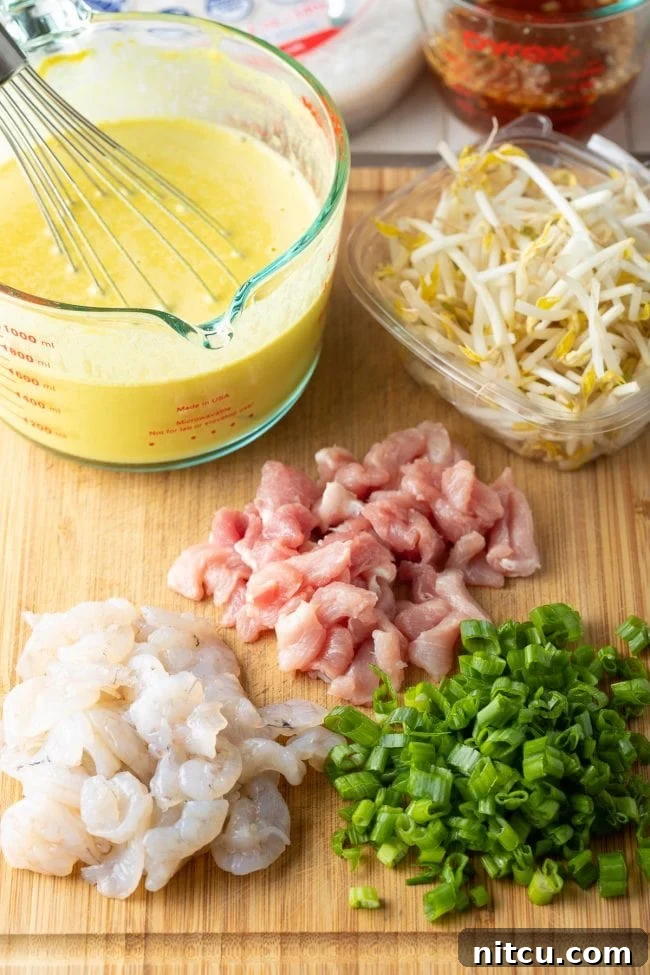 Recipe preparation scene showing neatly arranged piles of chopped chicken, shrimp, and green onions on a cutting board. A glass measuring cup holds a vibrant yellow Vietnamese crepe batter, with a package of fresh bean sprouts resting nearby, awaiting their turn.