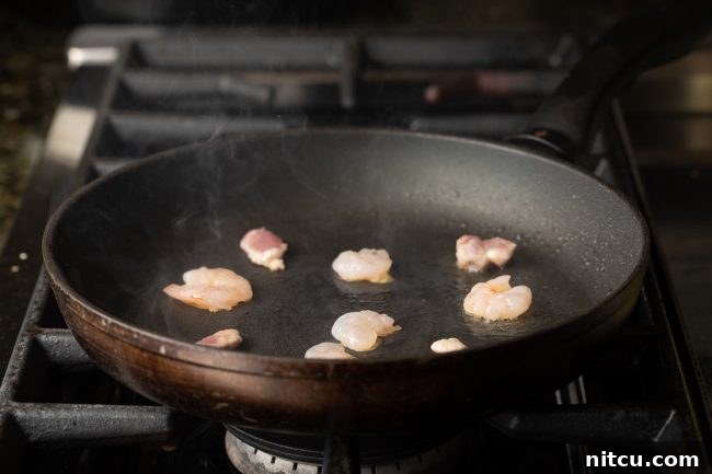 Close-up of fresh shrimp being cooked in a hot skillet with a small amount of oil, preparing for the Bánh Xèo filling.