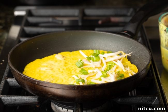 Freshly chopped green onions and crisp bean sprouts are carefully added to one half of a cooking Bánh Xèo crepe in a hot skillet, ready for folding.