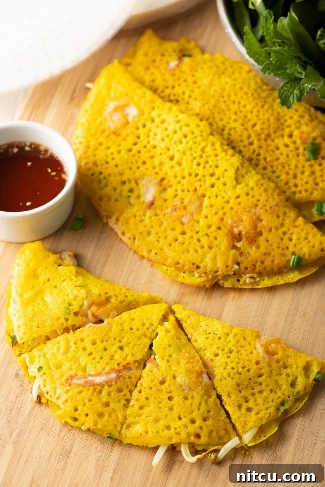 A top-down view of a cutting board displaying four perfectly cut triangles of golden, crispy Bánh Xèo, ready to be served or wrapped.