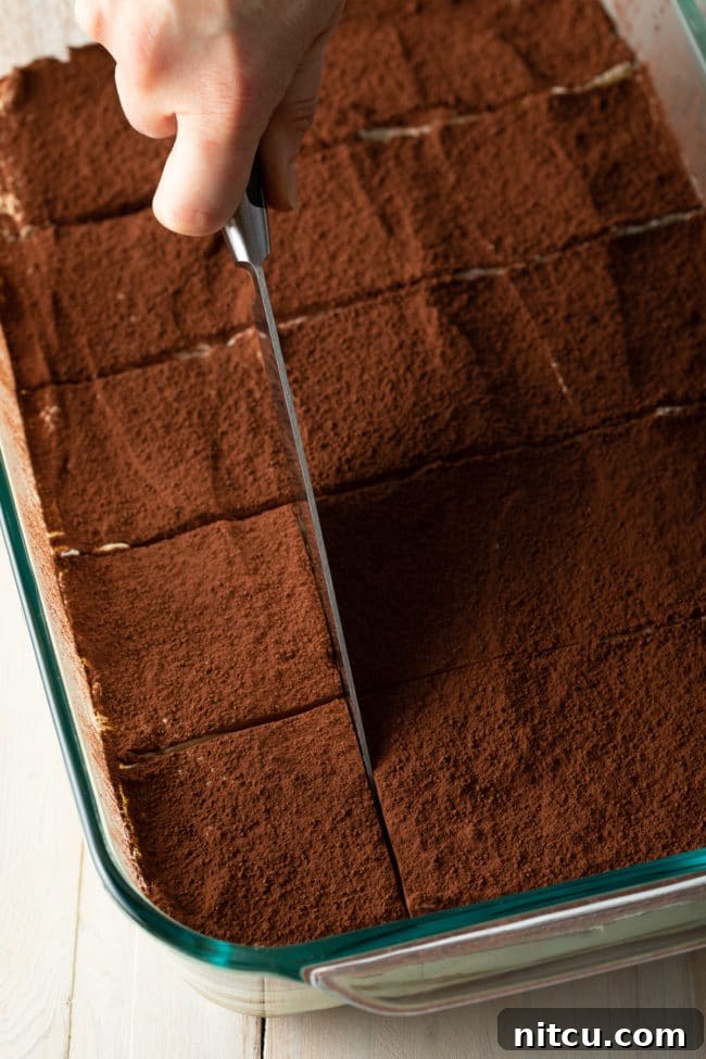 A hand holding a sharp knife, carefully slicing the easy tiramisu into neat squares, ready for serving.