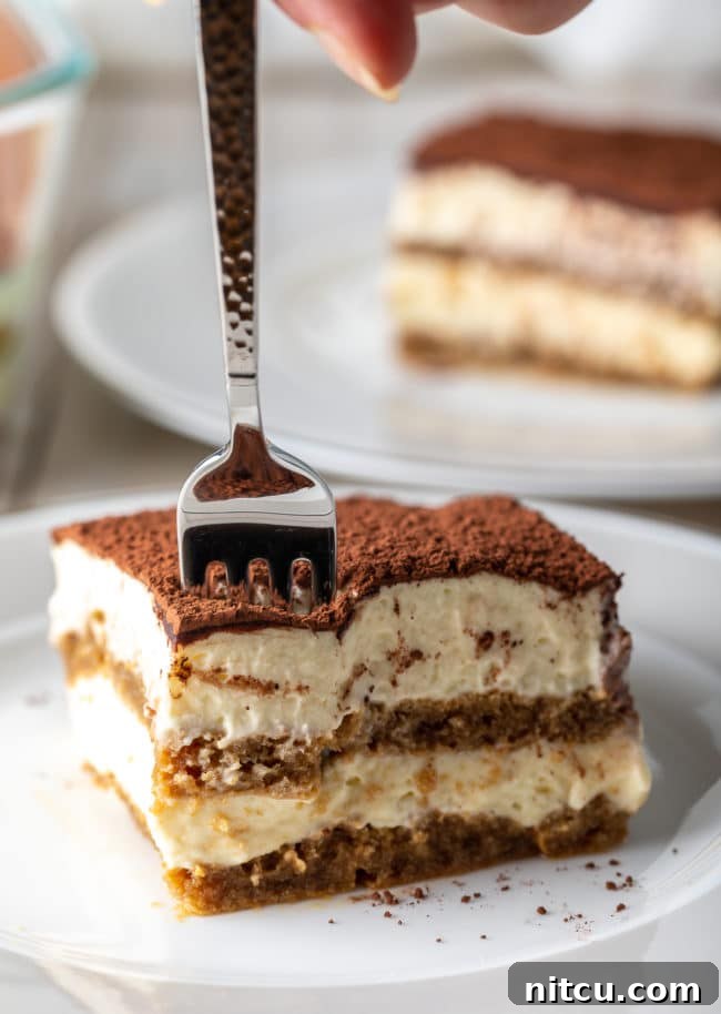 Easy Tiramisu Recipe - a beautiful slice on a plate with a fork gently breaking into the creamy layers.