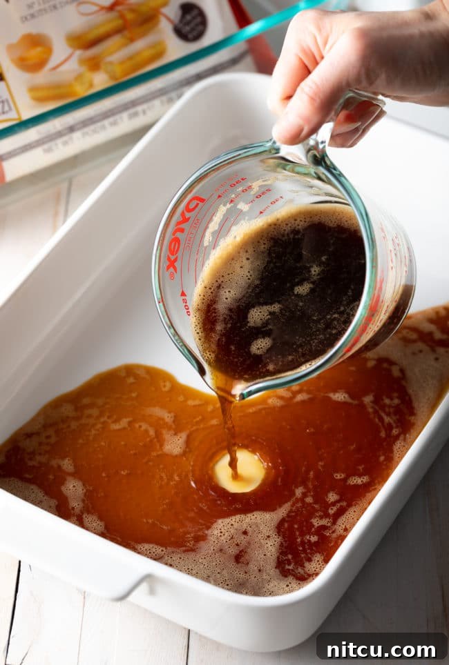 A hand carefully pouring freshly brewed espresso into a shallow dish, preparing the coffee bath for the ladyfingers.