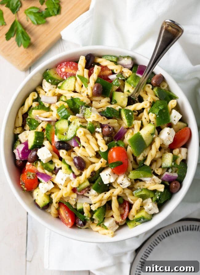 Fresh Greek Pasta Salad in a large bowl with a serving spoon, showcasing colorful vegetables and feta cheese.