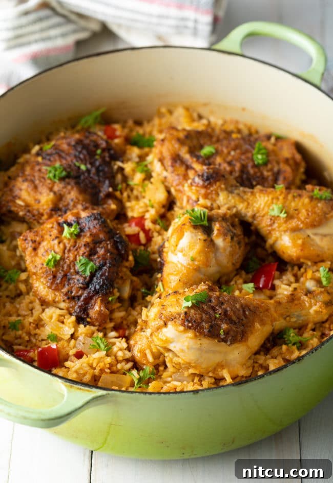 A generous serving of Arroz Con Pollo Cubano displayed in a rustic large Dutch oven, highlighting its rich color and texture.