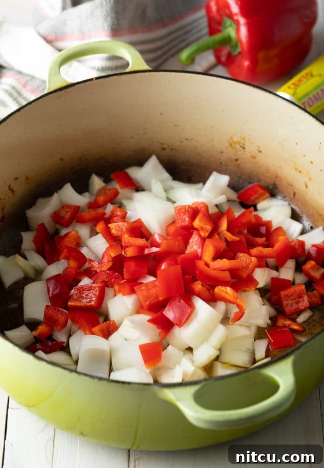 Chopped onions and red bell peppers gently sautéing in a Dutch oven, releasing their sweet aromas.