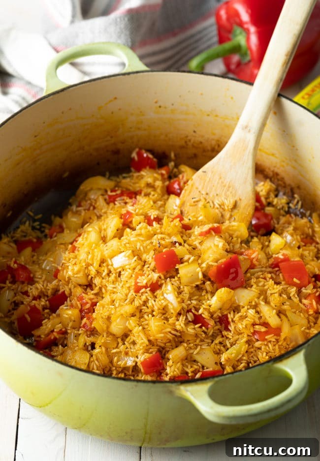 Long-grain rice being carefully mixed and sautéed with vegetables and seasonings in a Dutch oven, preparing for the liquid.
