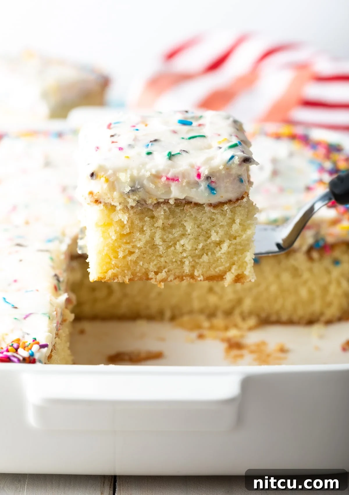 Spatula lifting a piece of perfectly baked vanilla birthday cake from a baking dish.