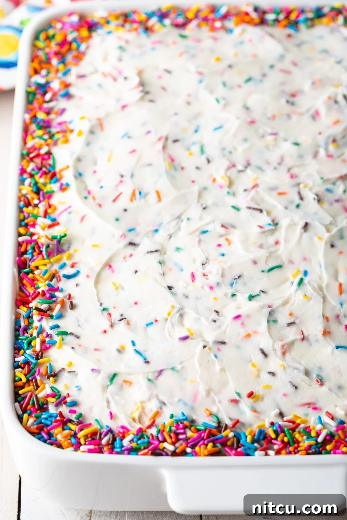 Vanilla birthday cake in a baking dish adorned with colorful sprinkles around the edges.