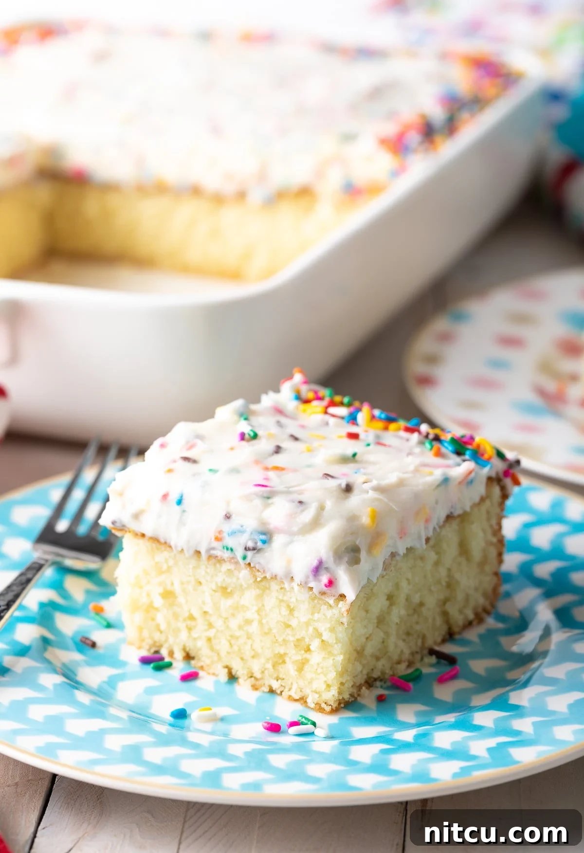 A delectable slice of homemade vanilla cake adorned with vibrant funfetti frosting, elegantly presented on a blue plate.