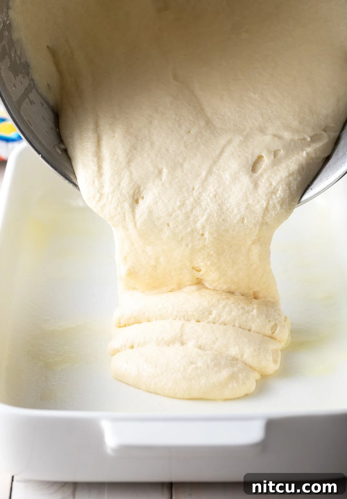 Cake batter being smoothly poured into a meticulously prepared baking dish.