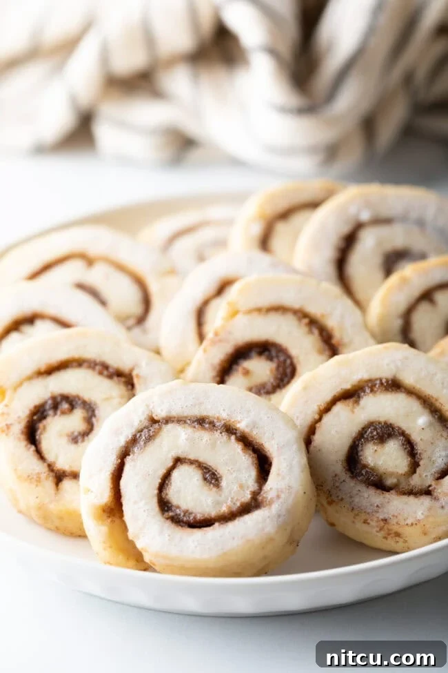 Close up of cinnamon roll cookies on plate, showing intricate swirls and delicate glaze