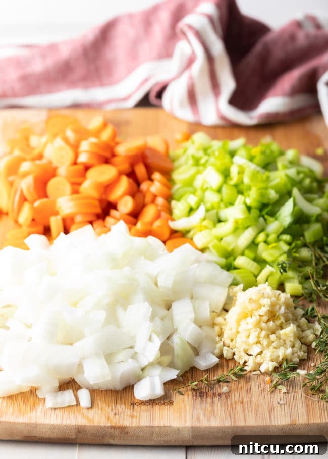 Chopped white onion, carrots, celery and garlic on a cutting board, prepared for cooking chicken and rice.