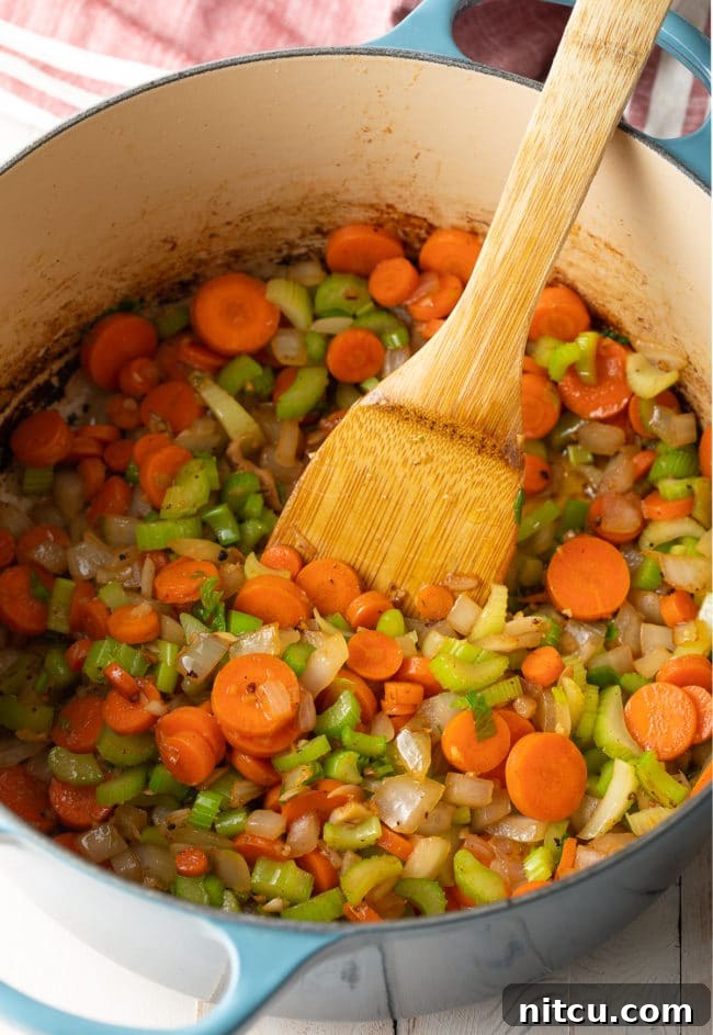 Sauteed vegetables (onions, carrots, celery, garlic) softening in a pot, creating an aromatic base.