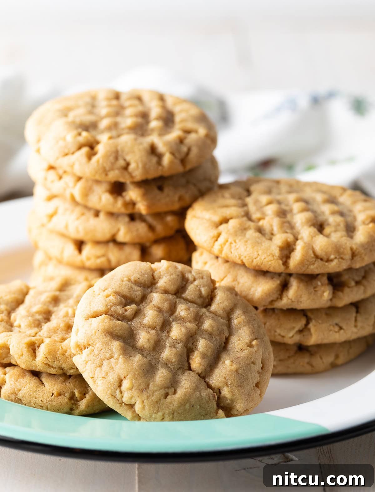 Three stacks of incredibly soft and chewy peanut butter cookies, perfectly baked with distinctive fork imprints on top, presented on a rustic plate.