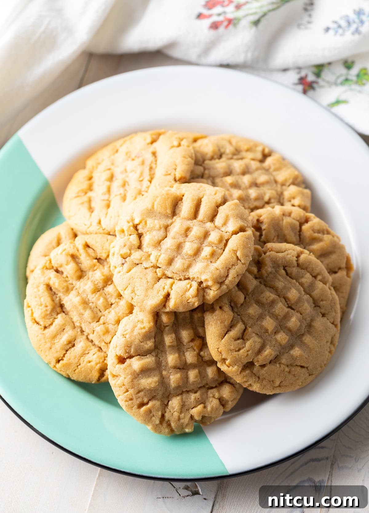 A plate piled high with chewy peanut butter cookies, showcasing their perfect golden-brown hue and rustic appearance, with a vibrant green and white backdrop.