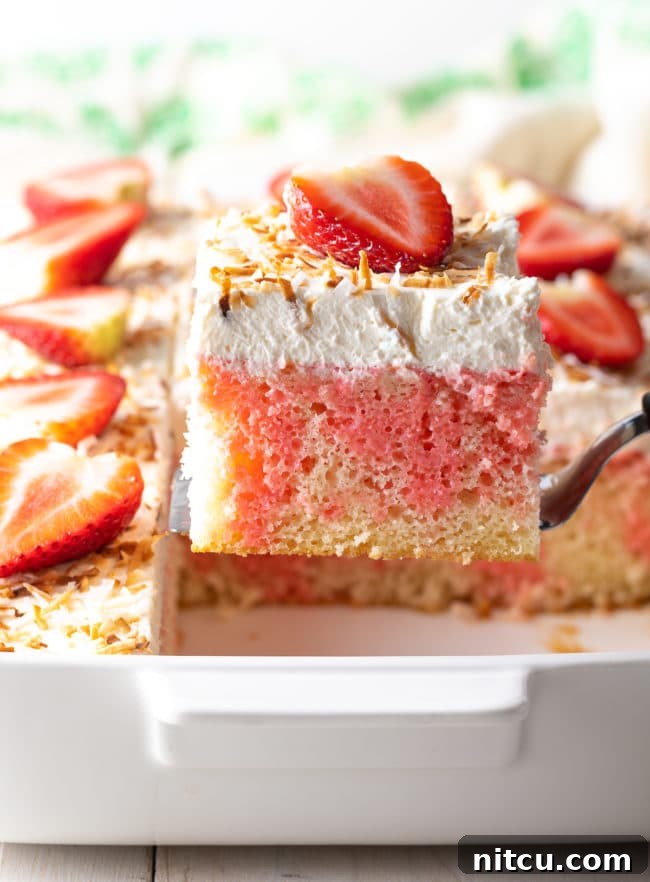 Strawberry Pineapple Jello Cake Recipe AKA Poke Cake - lifted out of the pan, showcasing its beautiful layers.