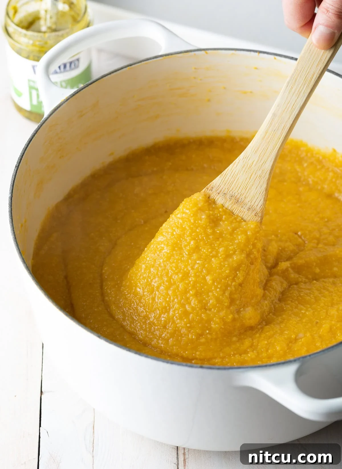 Cooked polenta simmering in a pot, being gently stirred with a wooden spoon to achieve a smooth and creamy texture.