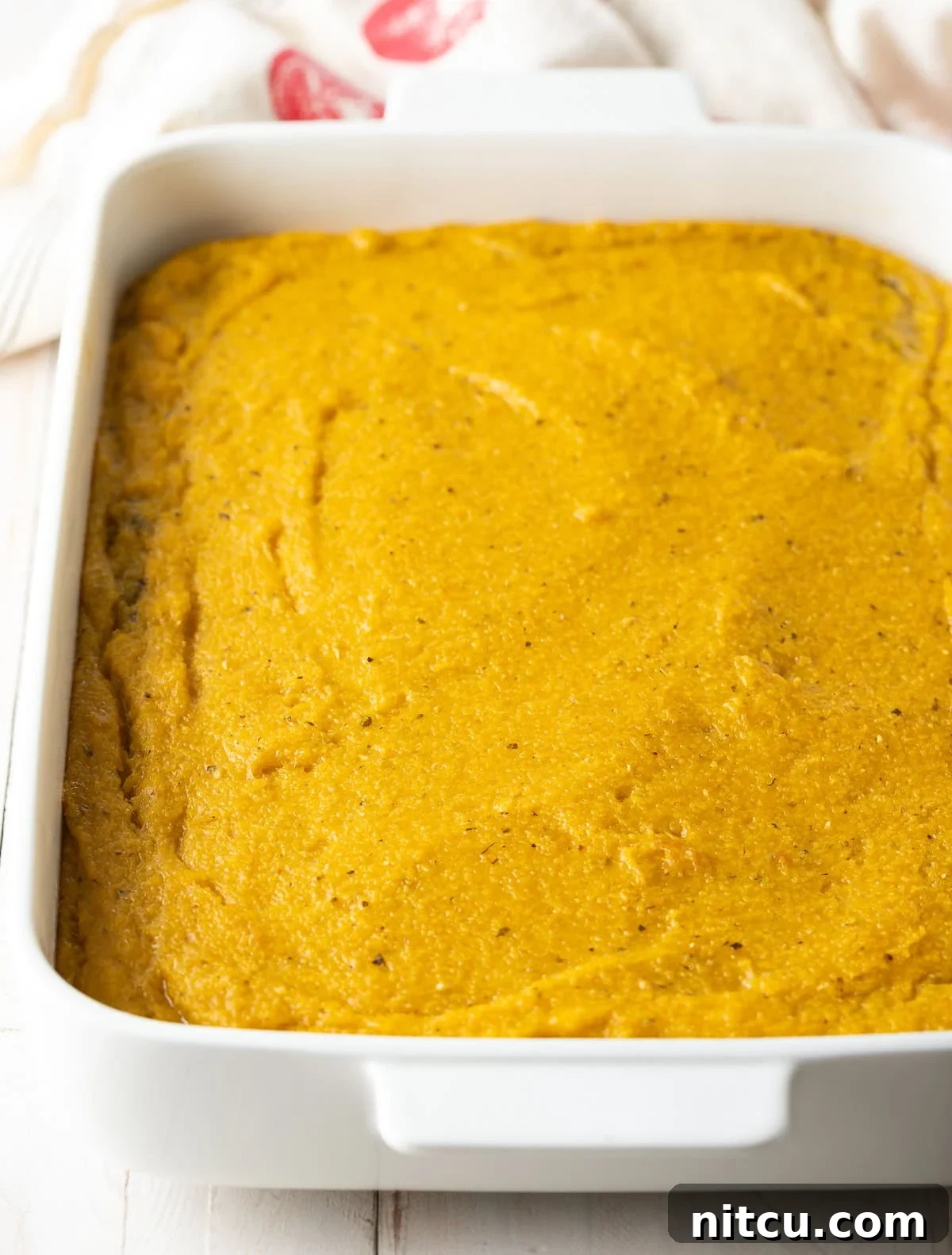 A thick, even layer of prepared polenta, infused with cheese and pesto, freshly poured into a baking dish, ready for its initial bake.