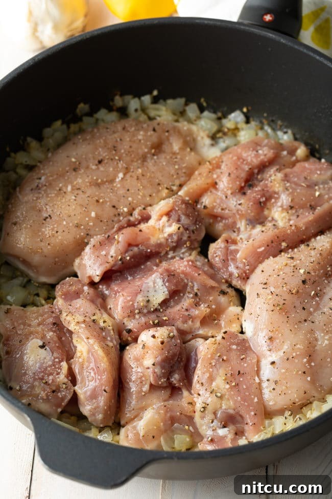 Chicken thighs seasoned and ready to be browned in a skillet with sautéed onions and garlic.