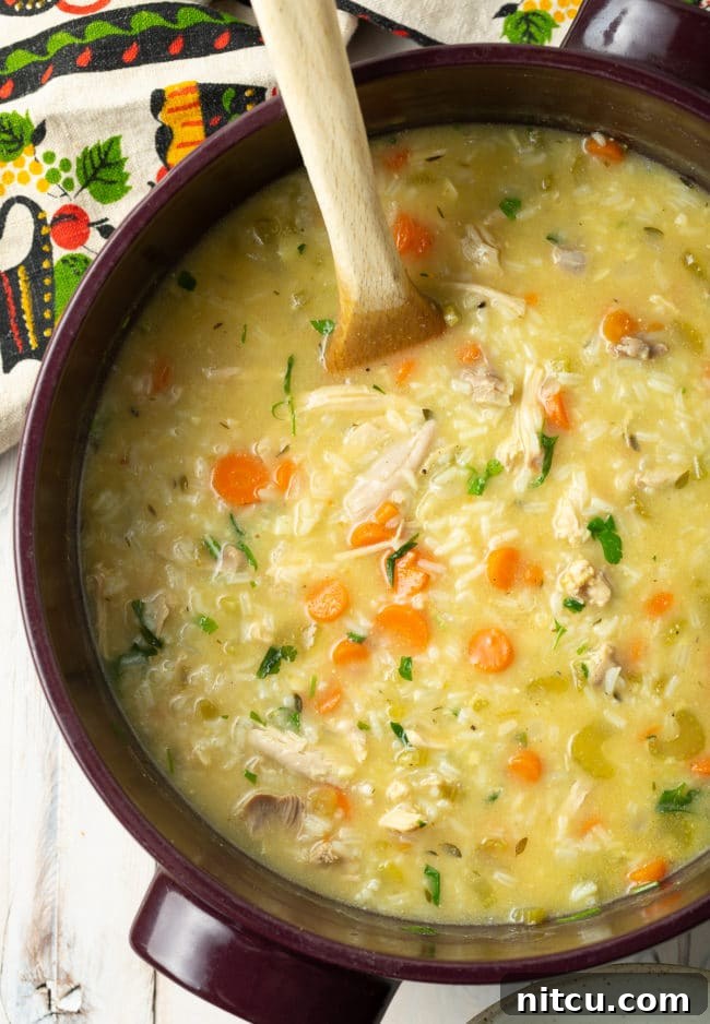 A whole pot of creamy chicken and rice soup with a wooden spoon, ready to serve.