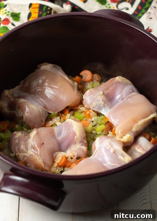 Chicken and various vegetables simmering in a large soup pot, creating the base for chicken and rice soup.