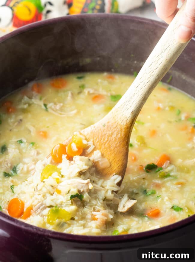 A wooden spoon stirring a pot of creamy chicken and rice soup, showing its rich texture.