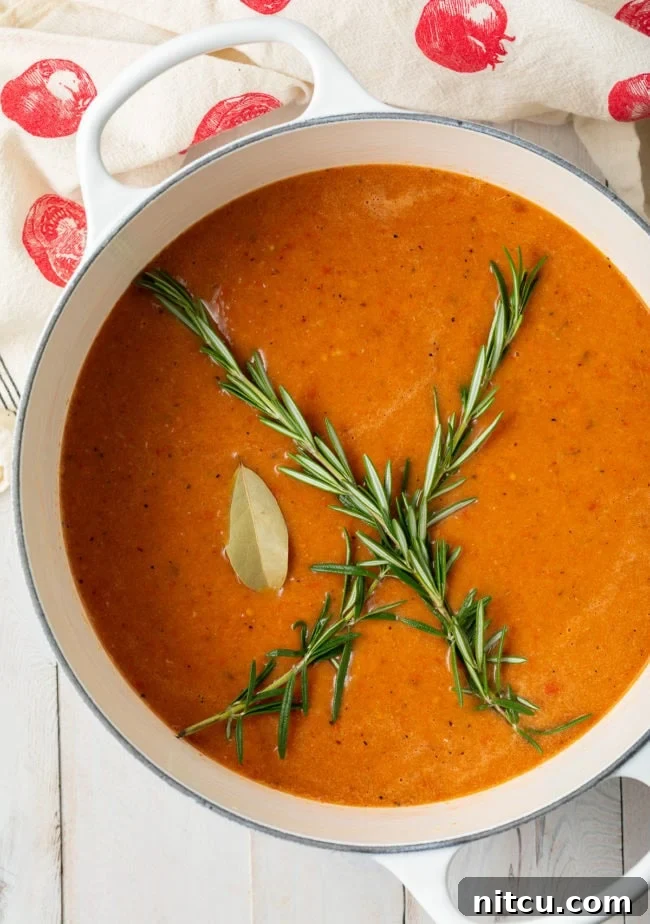Overhead shot of creamy roasted tomato soup in a large Dutch oven garnished with fresh basil sprigs.
