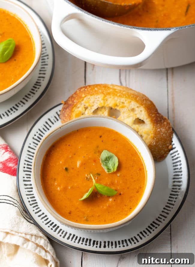 Two cozy bowls of creamy roasted tomato soup with a large pot of more soup in the blurred background, inviting warmth.