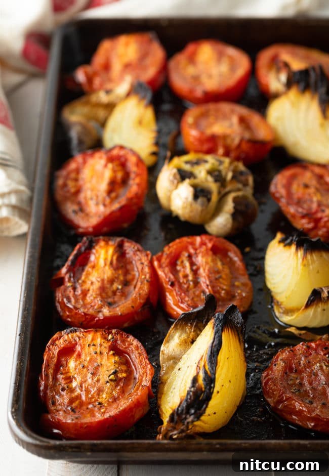 Roasted tomatoes, softened garlic cloves, and caramelized onion wedges on a baking sheet after being removed from the oven.