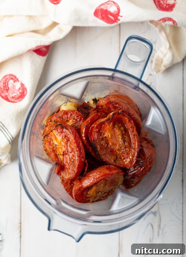 Roasted tomatoes, onions, and garlic being added to a blender for pureeing.