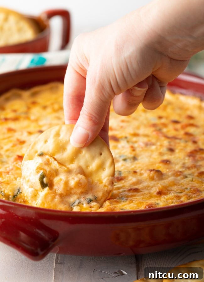 Hand scooping out hot shrimp dip with a cracker. 