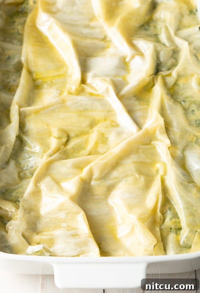 A close-up of the spinach pie's signature crinkled, golden-brown phyllo crust, shimmering with ghee after baking, promising a delightful crunch.