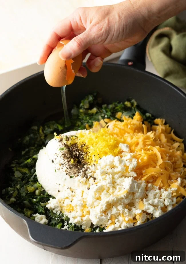 Top-down view of the sauté pan containing the cooked greens, now thoroughly mixed with the dairy ingredients and eggs, creating a rich and homogenous pie filling.