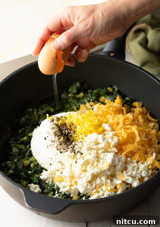 A bowl filled with a blend of creamy ricotta, shredded cheddar, and crumbled feta cheese, poised to be mixed into the herbaceous spinach filling.