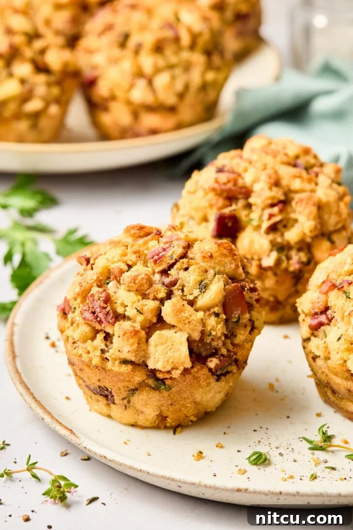 Close-up of golden brown Cornbread Stuffing Muffins with Apple and Pancetta on a rustic white plate, showcasing their crispy edges