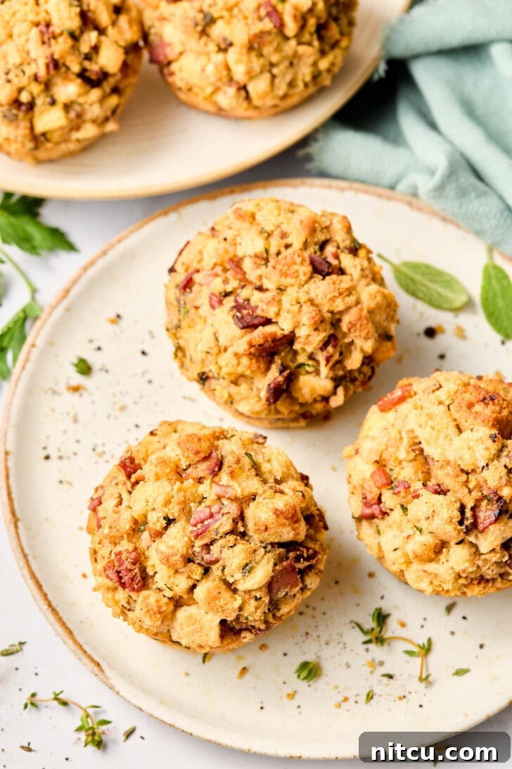 Several perfectly baked Cornbread Stuffing Muffins with Apple and Pancetta served on a white dinner plate, highlighting their appetizing golden crust and individual serving size