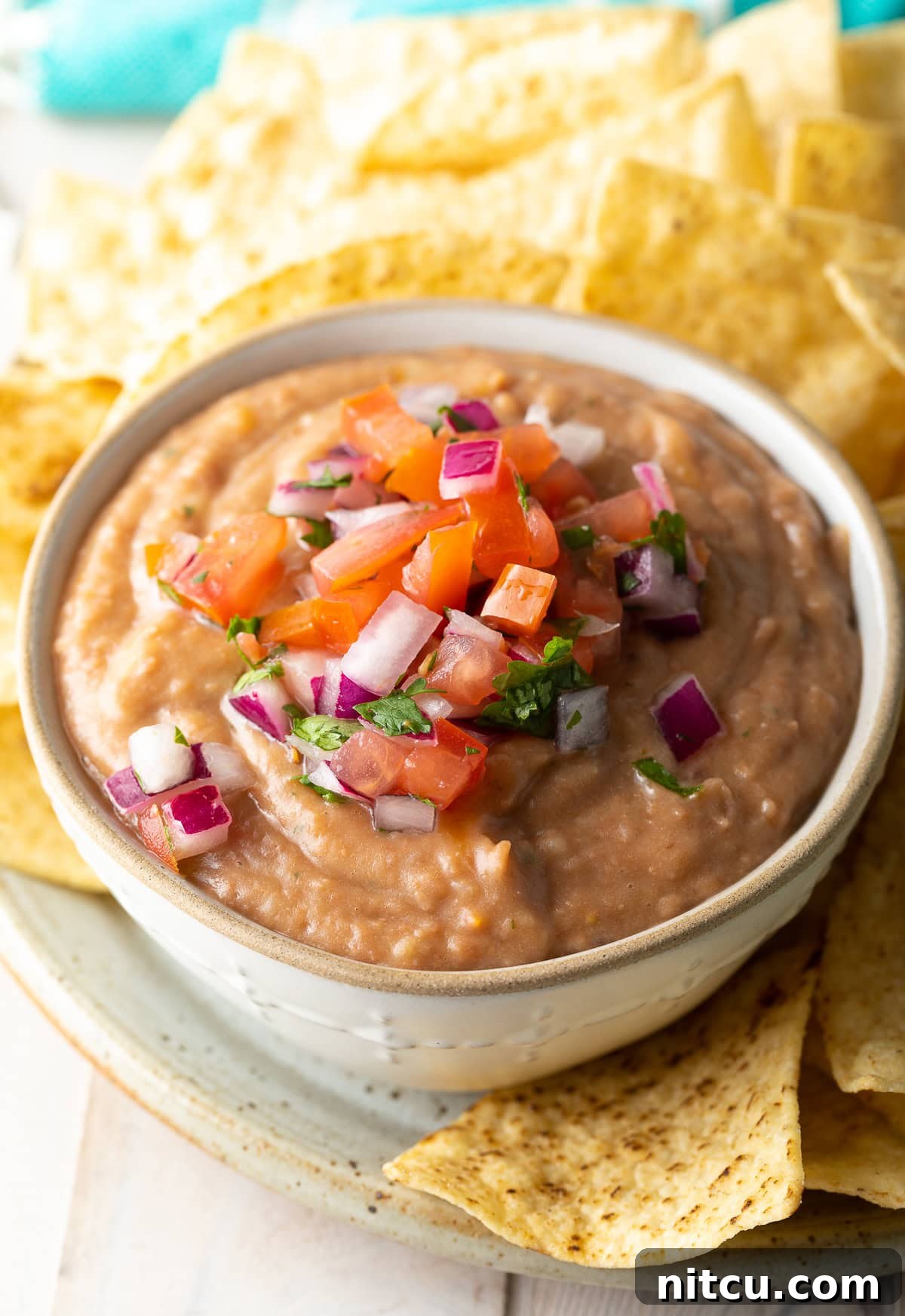 Creamy homemade bean dip, garnished with fresh pico de gallo and served with crunchy tortilla chips.