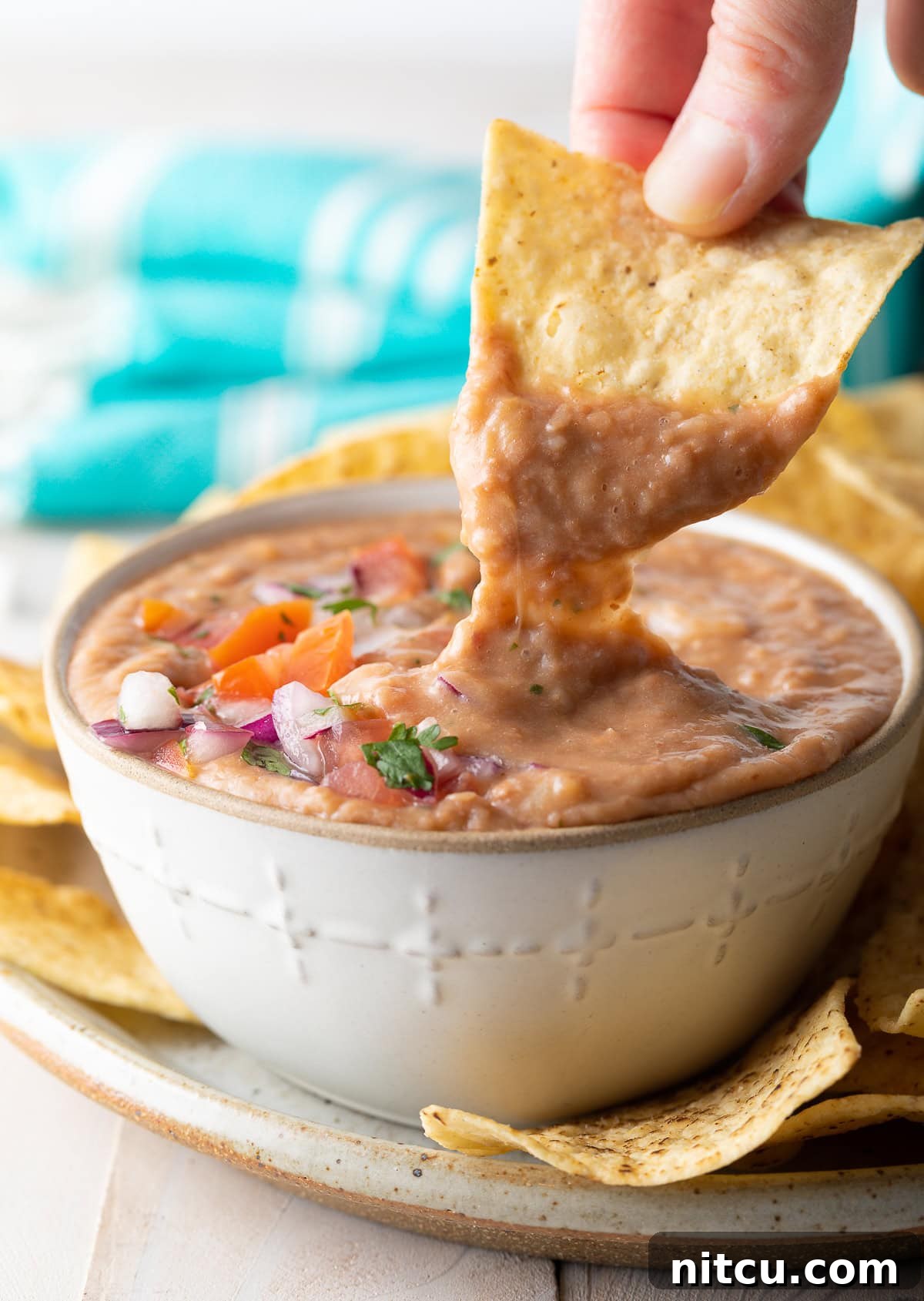 A close-up shot of a hand dipping a tortilla chip into a creamy, homemade bean dip, emphasizing its perfect scoopable texture.