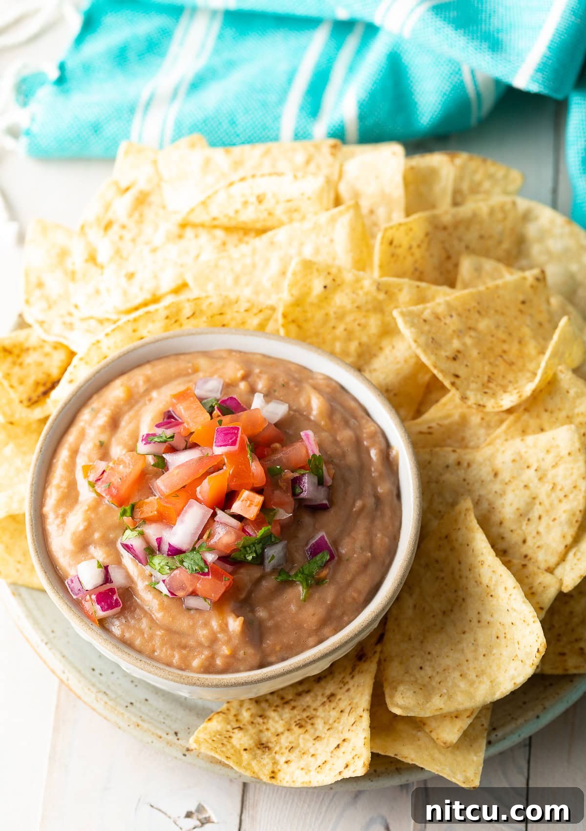 A bowl of rich pinto bean dip, topped with vibrant pico de gallo, served alongside a platter of crunchy tortilla chips, ready for snacking.