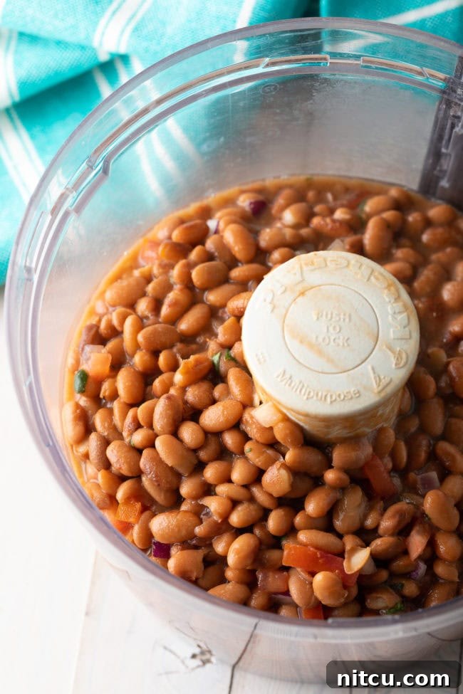 Pinto beans in a food processor bowl, before being blended into a smooth dip.