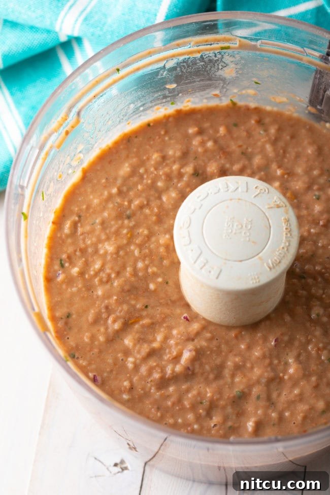 Food processor blending cooked pinto beans with other ingredients to create a smooth bean dip.