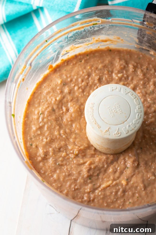Freshly blended bean dip being spooned into a serving bowl, ready for garnishing.
