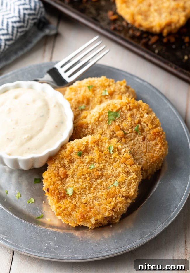 Three fried green tomatoes on a plate next to some sauce. 
