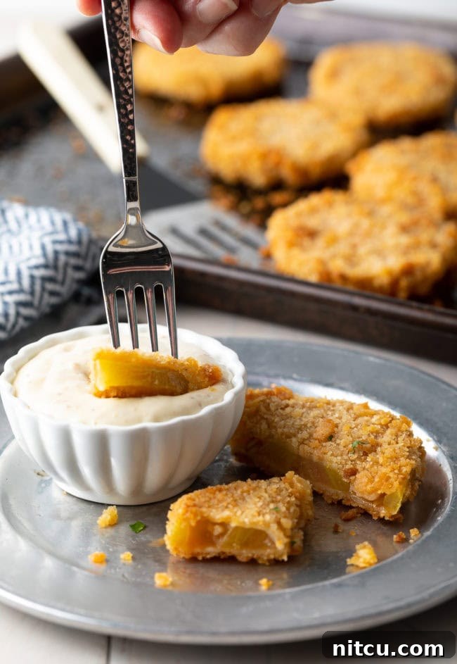 Fried green tomato on a plate cut into pieces with a fork dipping a piece into sauce. 