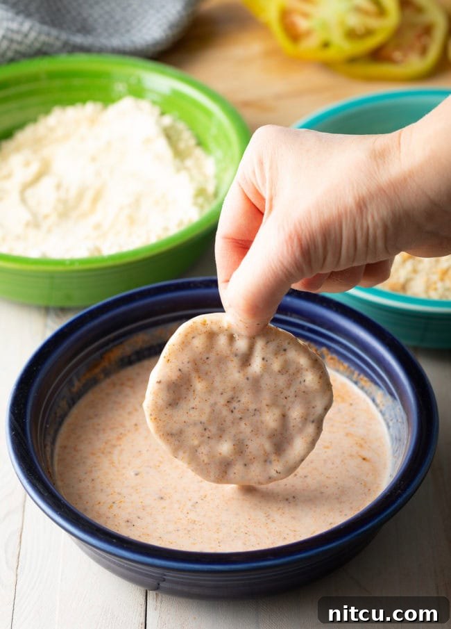 Hand dipping a green tomato slice into the buttermilk mixture. 